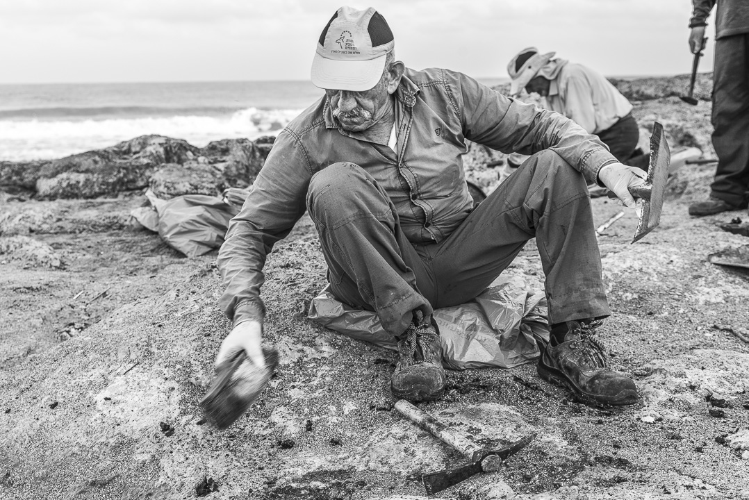 Alter Mann sitzt am Boden mit Bürste in Hand. Im Hintergrund Meer, schwarz/weiss Bild, Jacqueline Morgenroth Fotografie